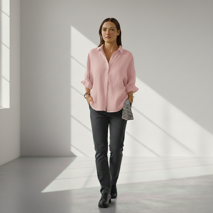 Woman wearing a pink shirt and dark pants in a bright room with sunlight filtering through.