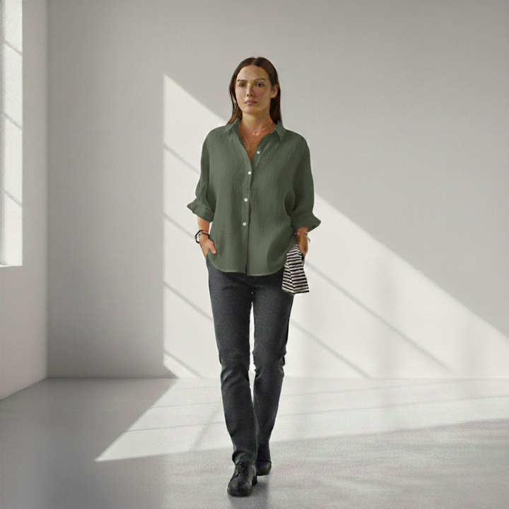 Woman wearing a green shirt and dark pants in a minimalistic room with light streaming through a window.