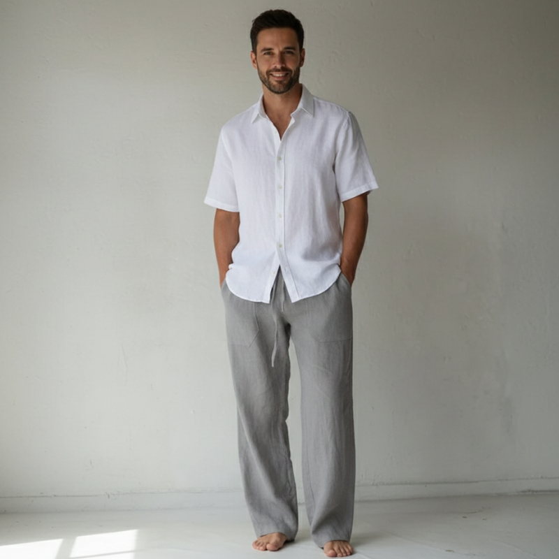 Man wearing a white shirt and gray pants standing against a plain background