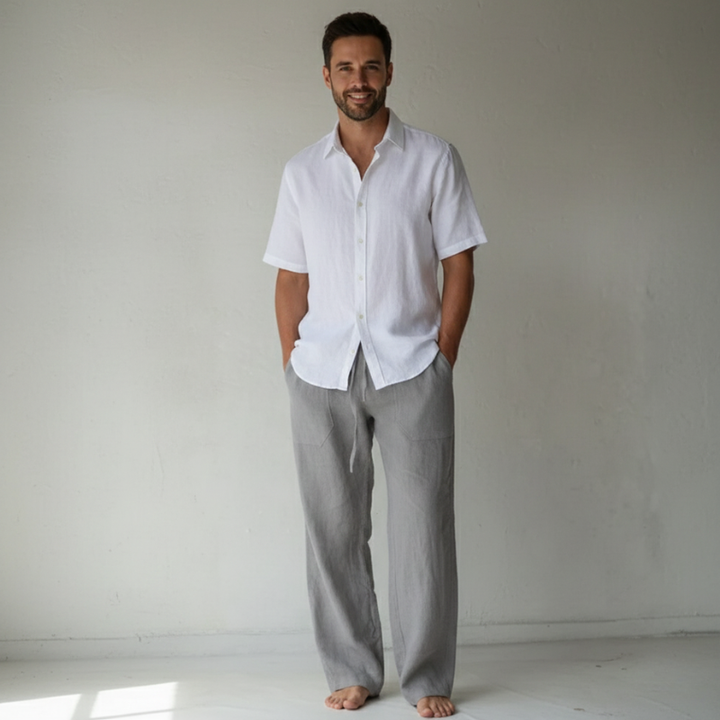 Man wearing a white shirt and gray pants standing against a plain background