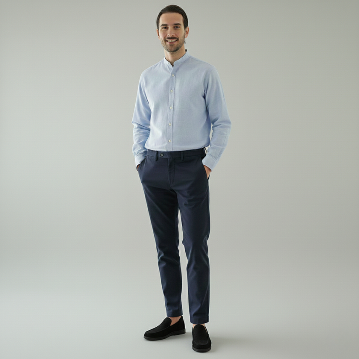 Man wearing a light blue shirt and dark pants against a plain background