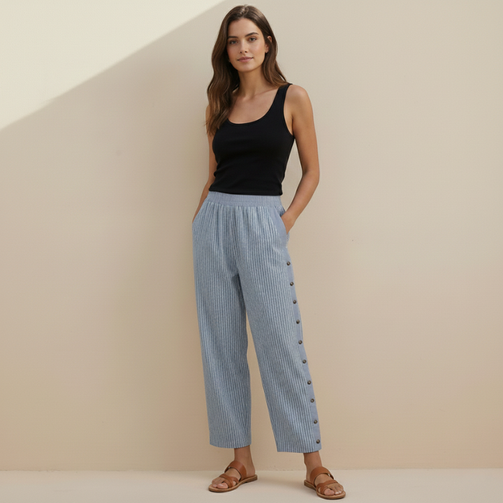 Woman wearing a black tank top and blue striped pants with buttons on a beige background