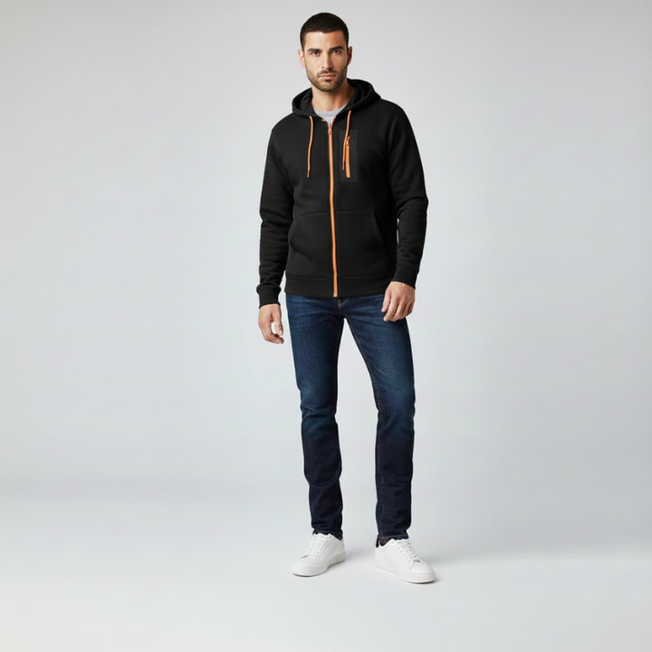 Man wearing a black hoodie with an orange zipper, blue jeans, and white sneakers on a light gray background