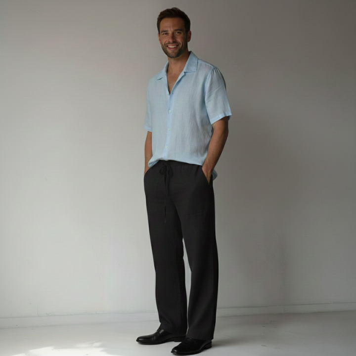 Man wearing a light blue shirt and black pants against a plain background