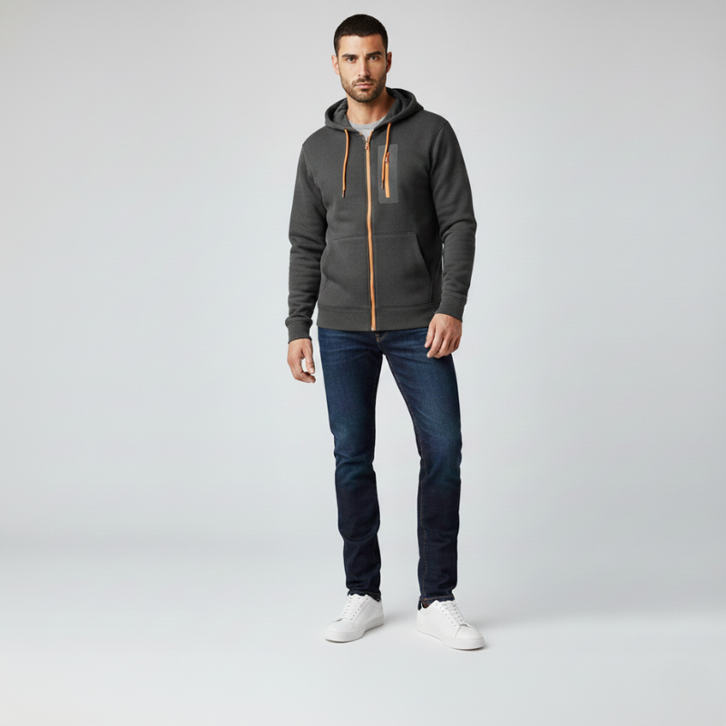 Man wearing a gray hoodie with an orange zipper, dark jeans, and white sneakers on a light gray background