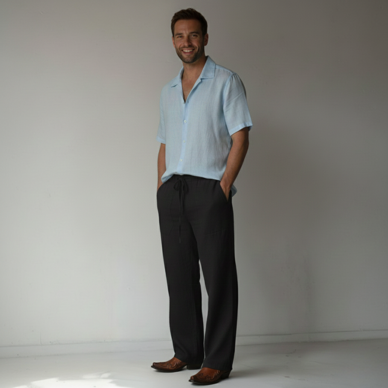 Man wearing a light blue shirt and dark pants against a plain background