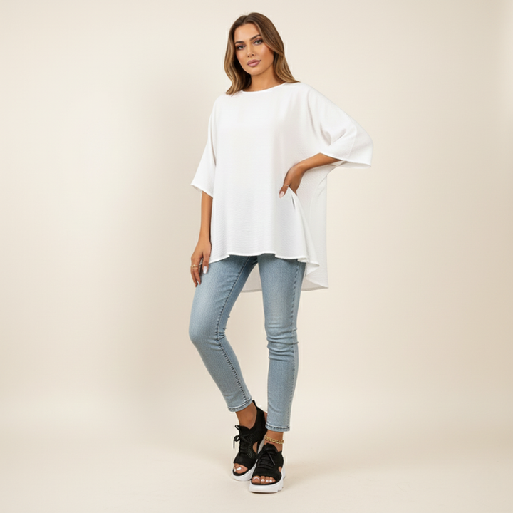 Woman wearing a white oversized shirt and light blue jeans on a beige background
