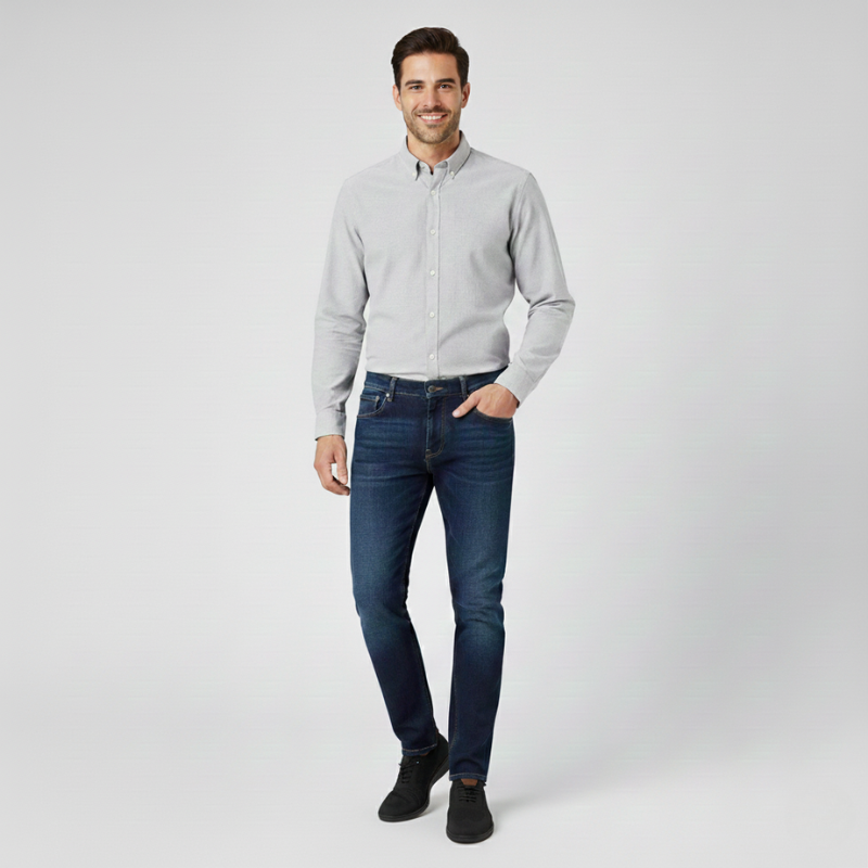 Man wearing a light gray button-up shirt and dark blue jeans on a white background