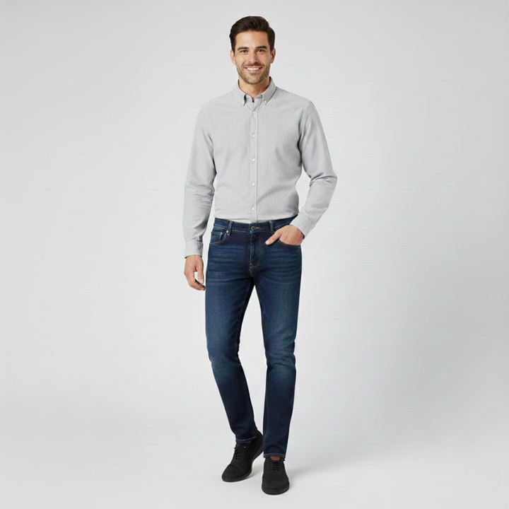 Man wearing a light gray button-up shirt and dark blue jeans on a white background
