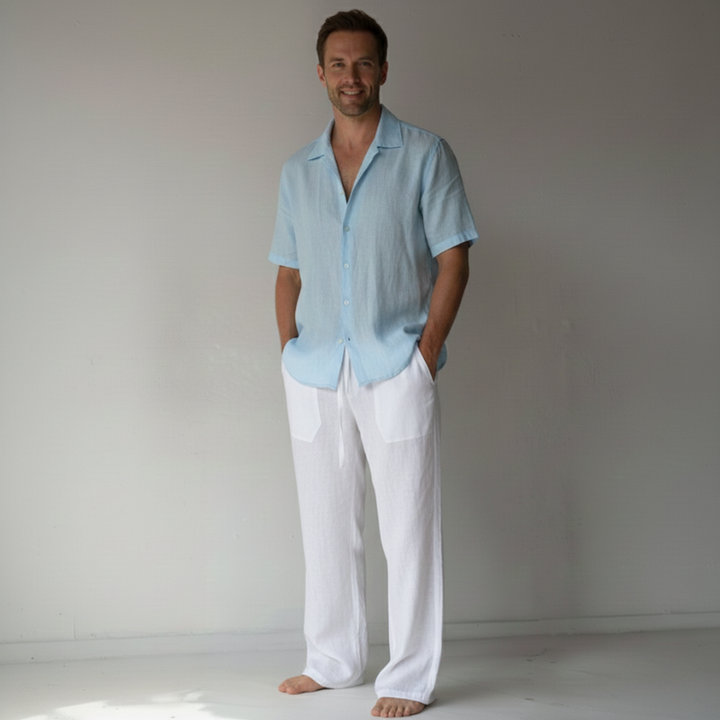 Man wearing a light blue shirt and white pants against a plain background