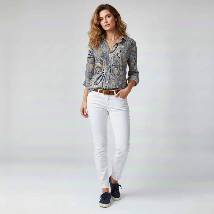 Woman wearing a patterned shirt and white pants on a plain background