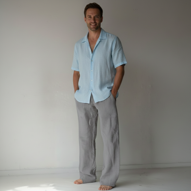 Man wearing a light blue shirt and gray pants standing against a plain white background