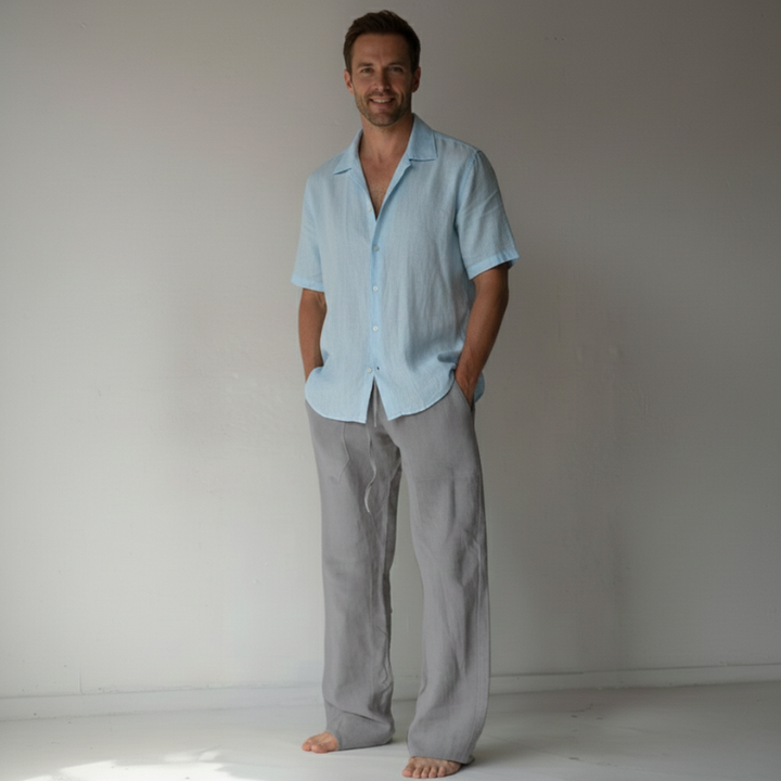 Man wearing a light blue shirt and gray pants standing against a plain white background
