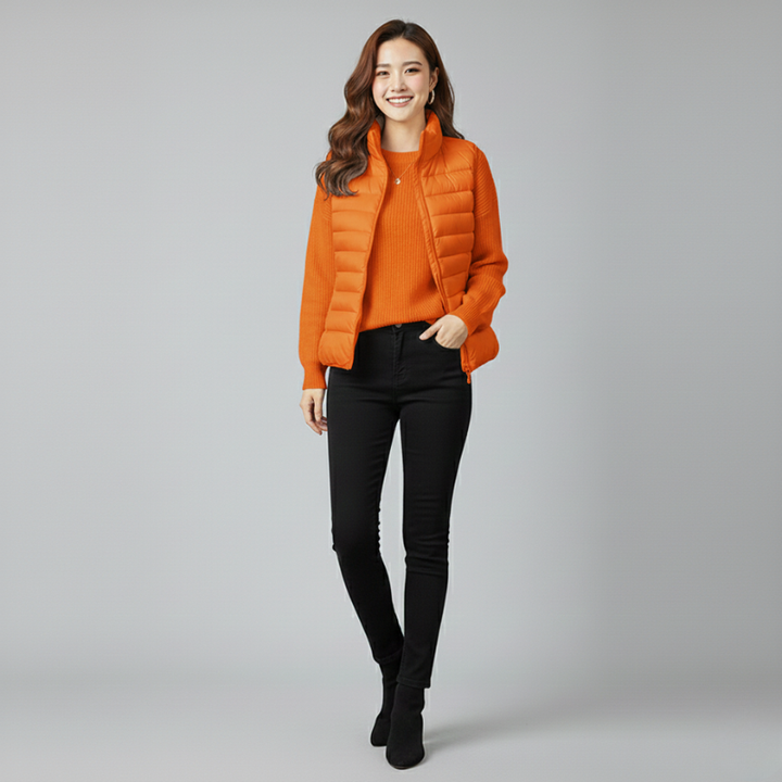 Woman wearing an orange puffer jacket and black pants on a gray background