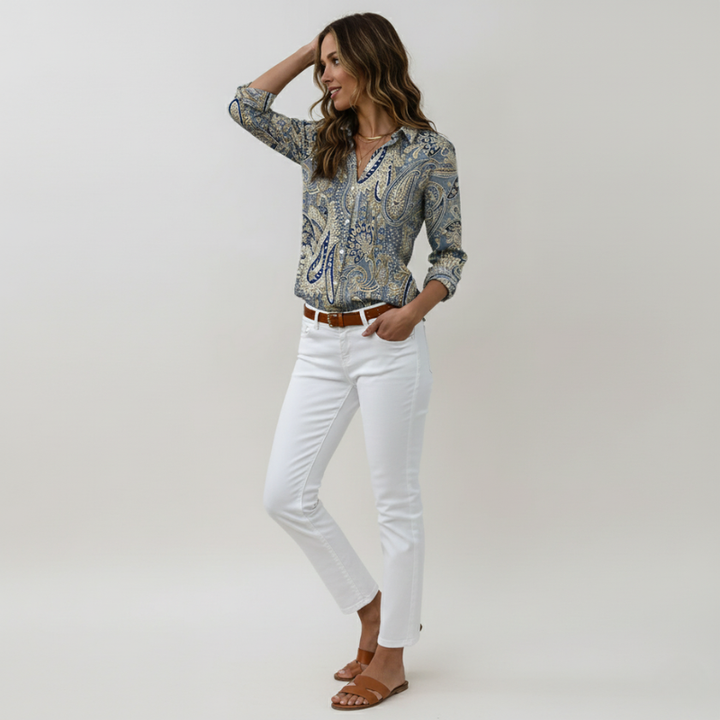 Woman wearing a patterned shirt and white pants on a plain background