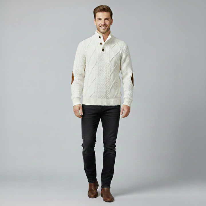 Man wearing a cream sweater and dark pants on a gray background