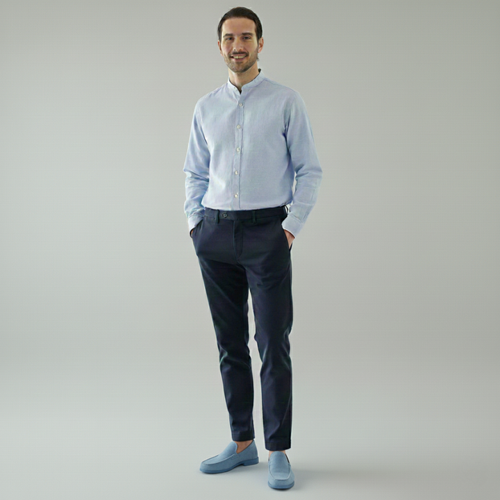 Man wearing a light blue shirt and dark pants on a plain background