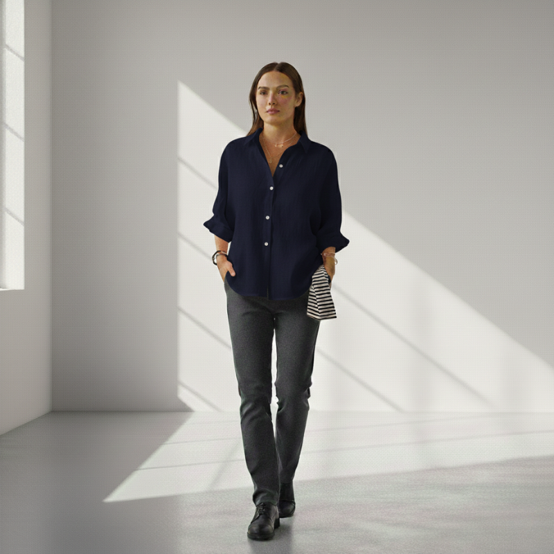 Woman wearing a navy shirt and gray pants in a minimalistic room with light streaming through windows.