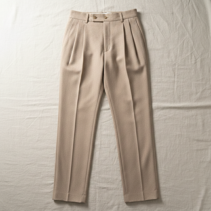 Flatlay of beige tailored dress pants displaying pleats, waistband structure, and clean fabric texture.