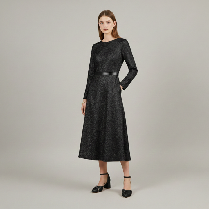 Model wearing a black long sleeve midi dress with a defined waist, paired with black block heel ankle strap shoes in a studio setting.