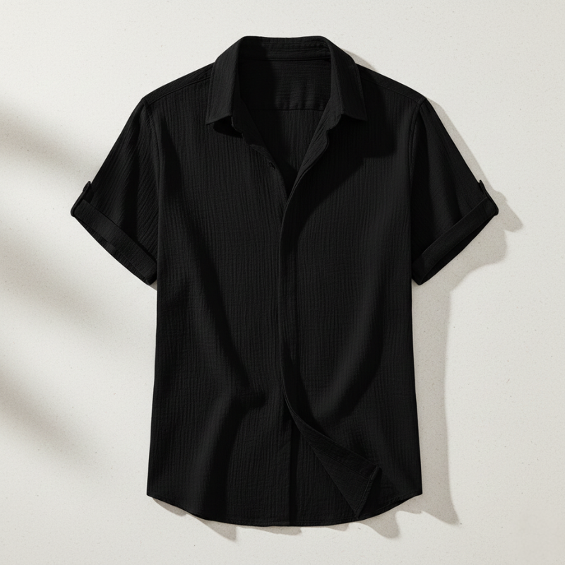 Flatlay of a black men’s short-sleeve button-up shirt with a relaxed collar on a neutral background.