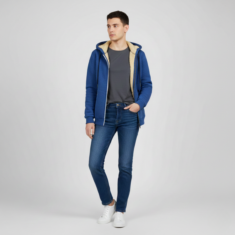 Side view of a man wearing a blue sherpa lined hoodie with blue jeans and white sneakers, standing with one hand in pocket.