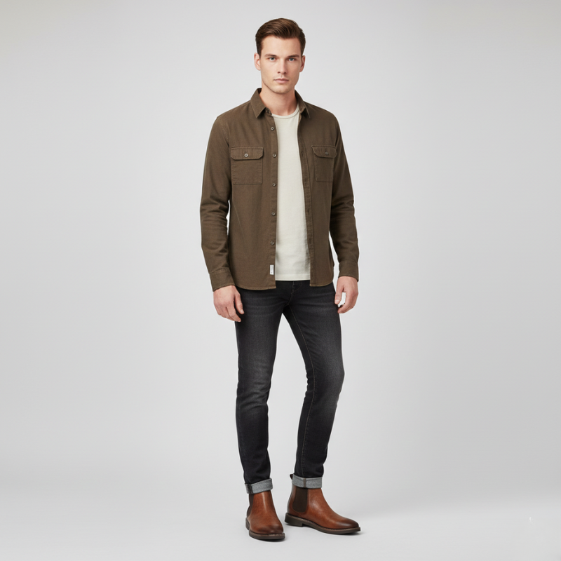 Man wearing a brown jacket, white shirt, black jeans, and brown boots on a light gray background