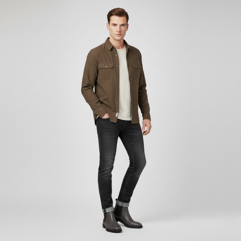 Man wearing a brown jacket, white shirt, black jeans, and dark shoes on a light gray background