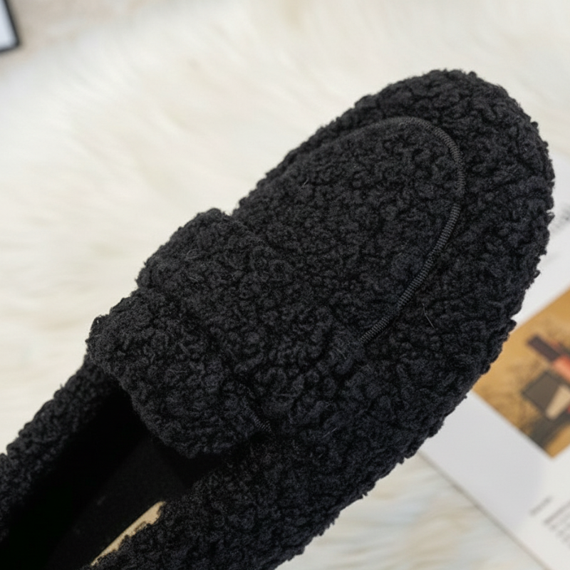 Black fuzzy slippers on a light wooden floor