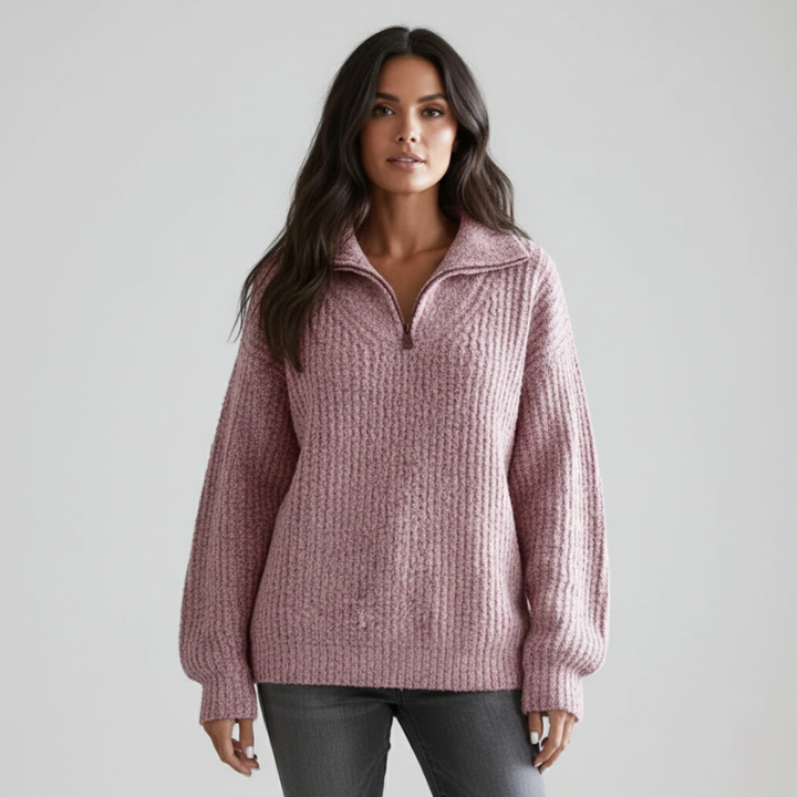 Model trägt einen rosa Strickpullover mit funktionalem Reißverschlusskragen und weichem Maschenbild in heller Innenraumszene.