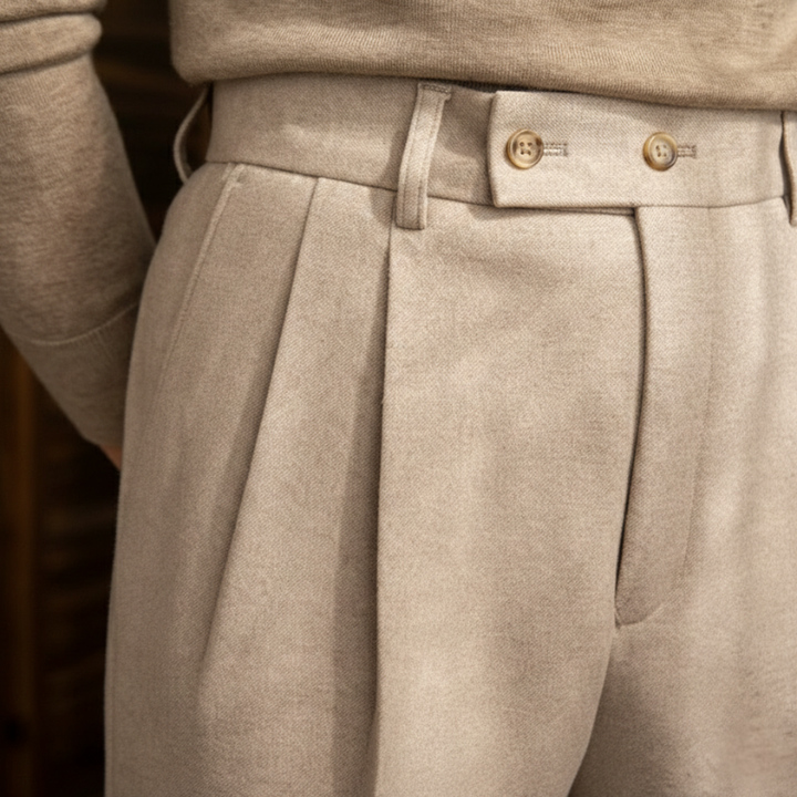 Close-up of beige dress pants showing pleats, waistband stitching, and button closure.