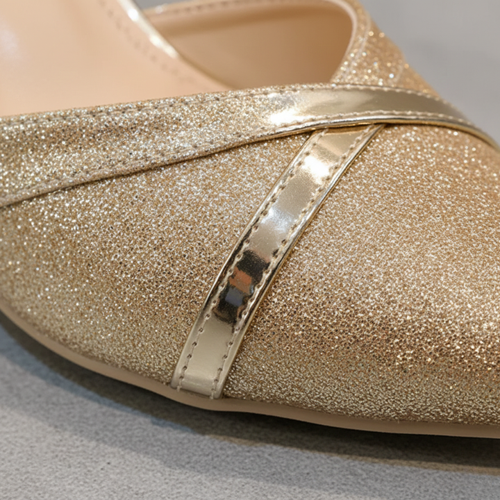Close-up of a glittery gold shoe with a strap on a gray background
