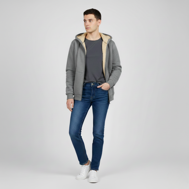 Side view of a man wearing a gray sherpa lined hoodie with blue jeans and white sneakers, standing with one hand in pocket.