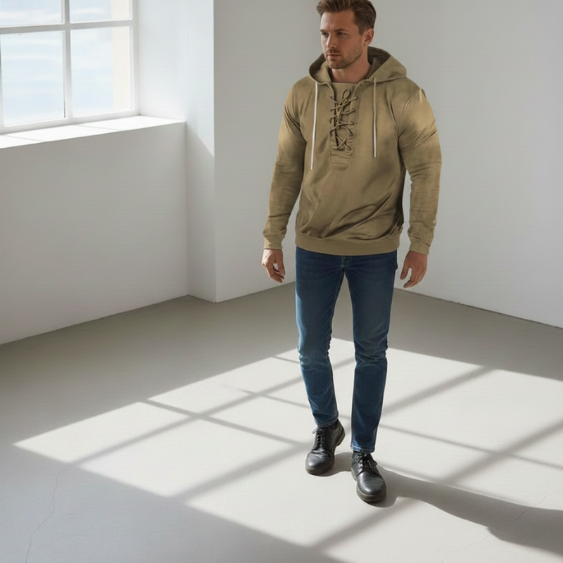 Model trägt einen khakifarbenen Hoodie mit entspanntem Schnitt und sportlichen Details in einem hellen Innenraum.