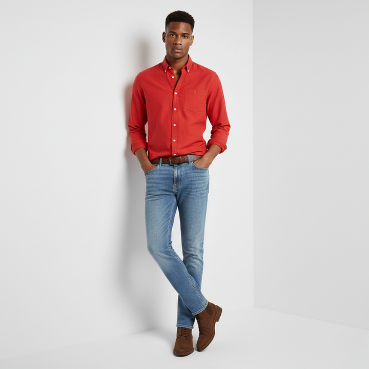 Man wearing a red shirt, blue jeans, and brown shoes against a white background