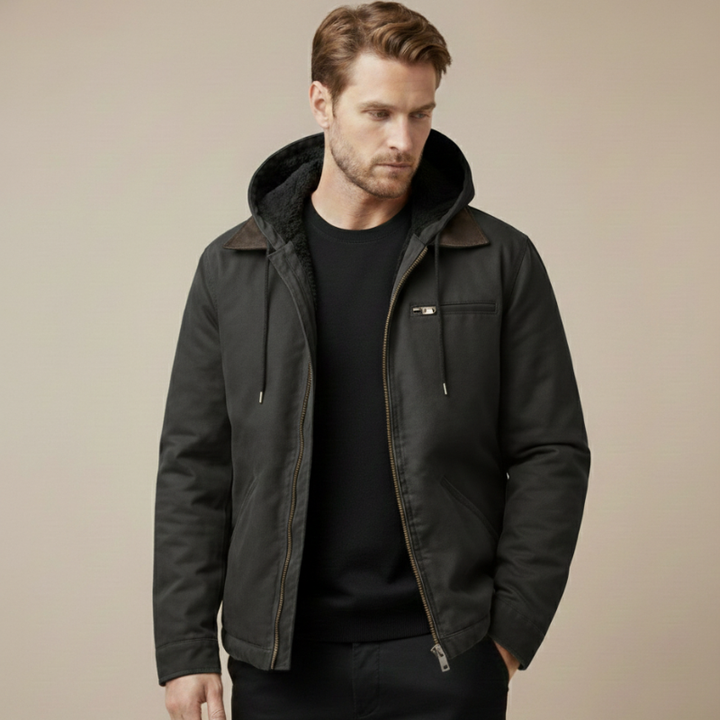 Man wearing a black hooded work jacket with a zip front and utility pockets in a neutral studio setting.