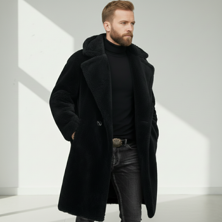 Man wearing a long black wool coat with structured shoulders and high collar in studio lighting.
