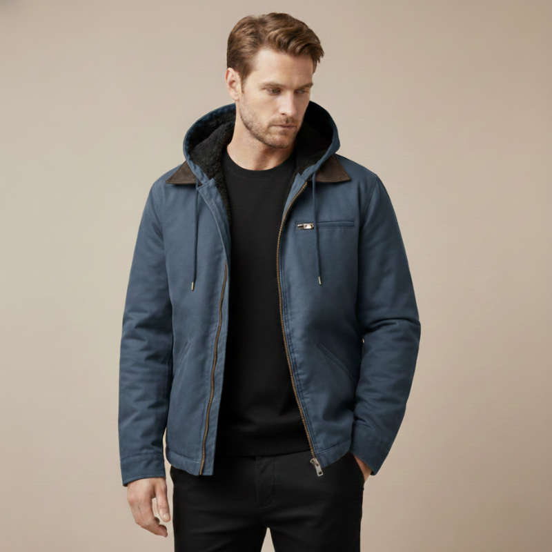 Male model wearing a blue canvas work jacket with a hood and zip closure styled over a dark shirt.