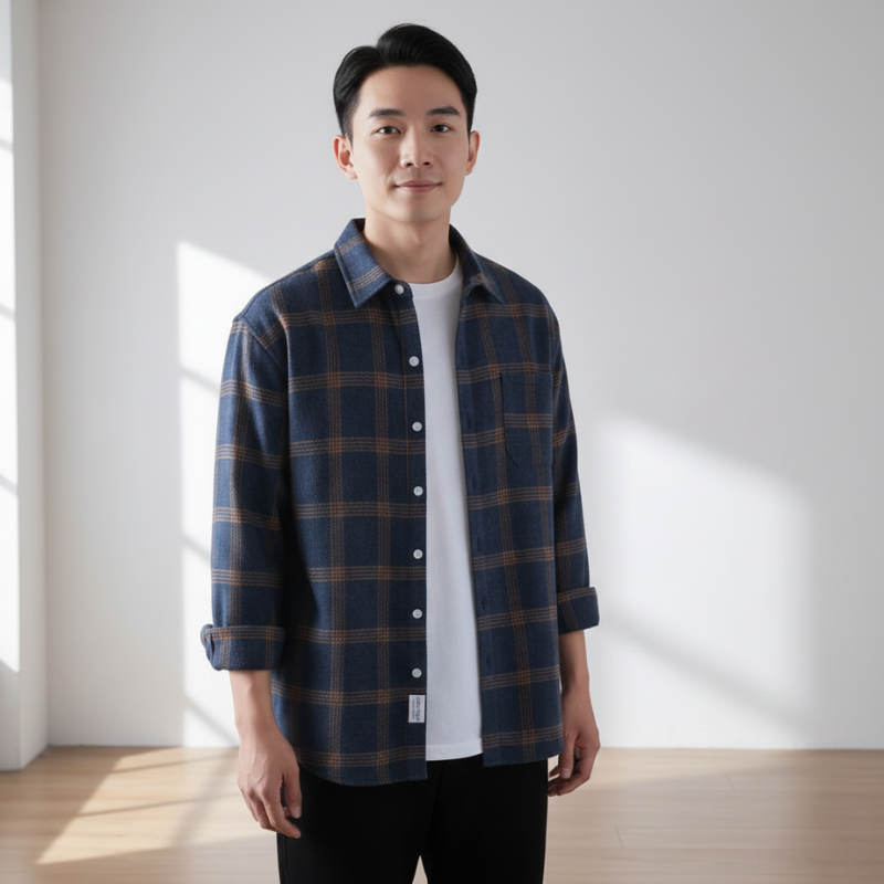 Full-body photo of a man wearing a blue plaid button-up shirt with black pants in natural room lighting.