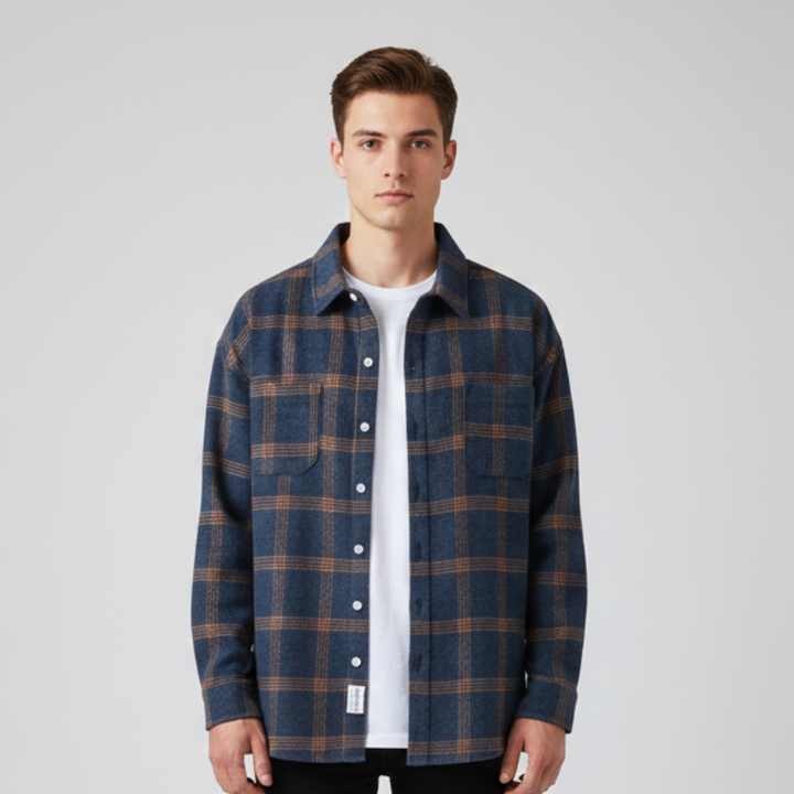 Man wearing a blue plaid flannel shirt over a white tee, standing in a clean studio setting.