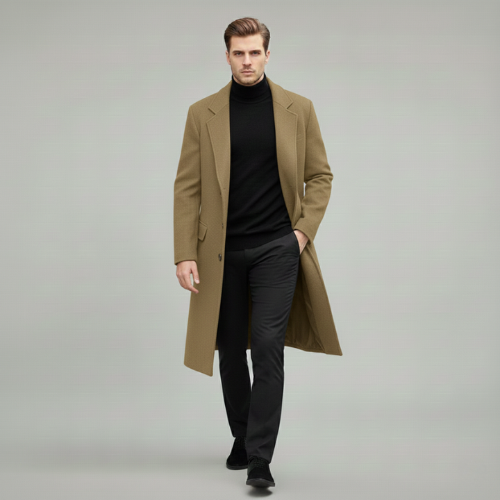 Man wearing a long brown coat over a black outfit on a gray background