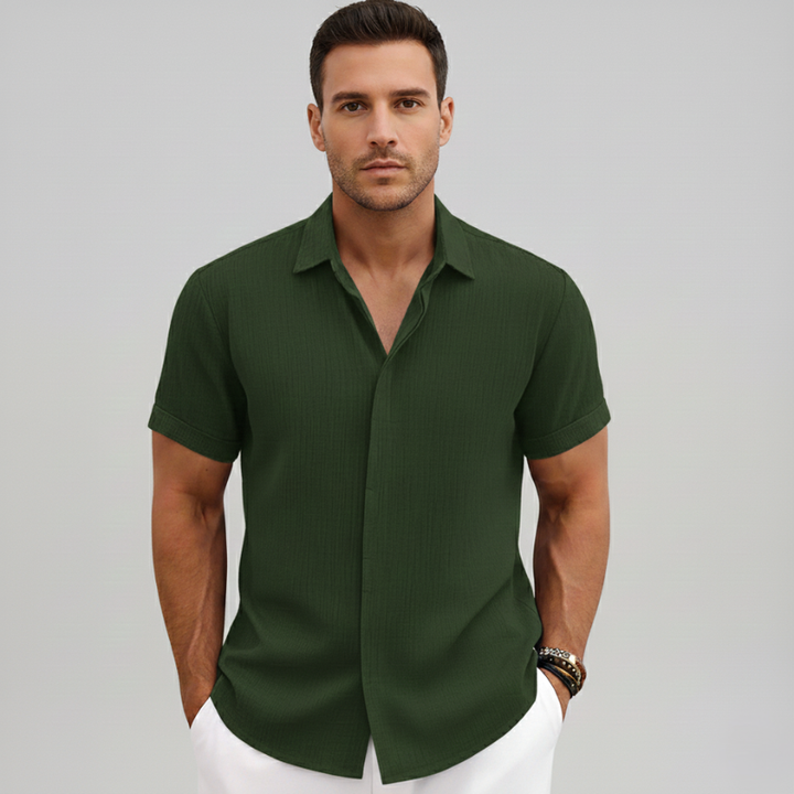 Male model in a green short-sleeve button-up shirt styled casually with white trousers.