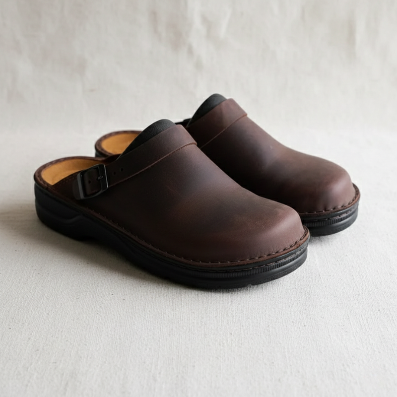 Man standing indoors wearing a patterned knit cardigan with dark pants in natural lighting.