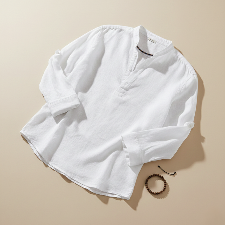 Flatlay of a white linen button-down shirt on a beige surface showing texture and stitching details.