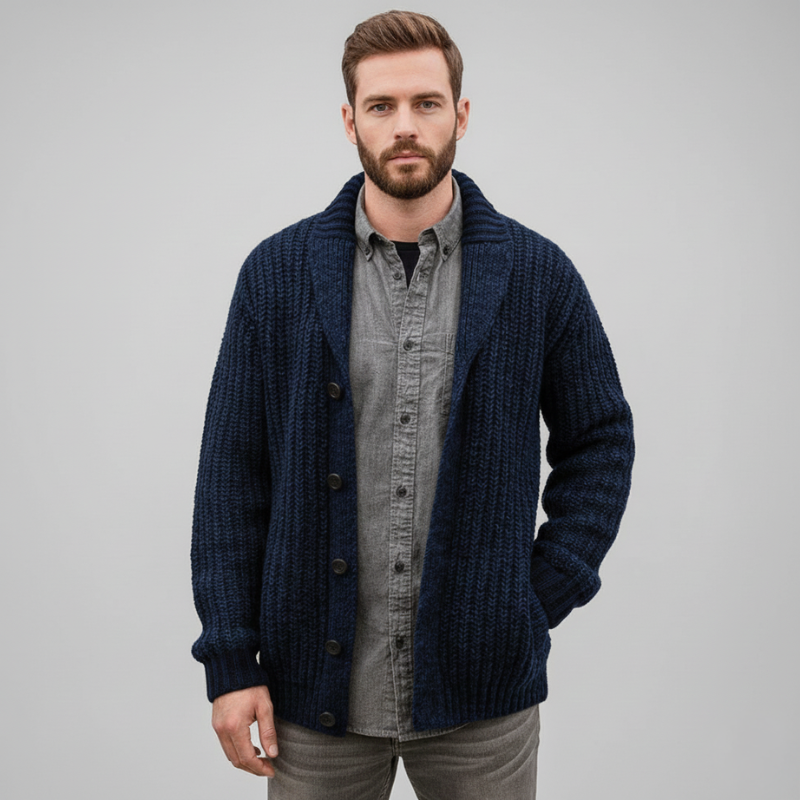 Man wearing a navy chunky knit cardigan layered over a gray shirt in studio lighting.