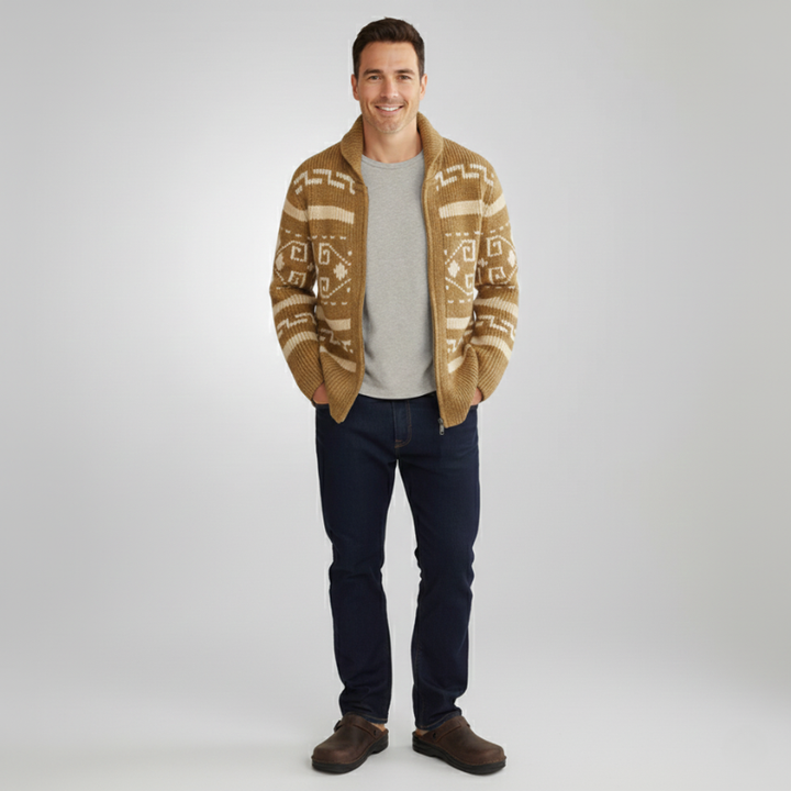 Man wearing a patterned knit cardigan layered over a white t-shirt with dark jeans in a studio setting.