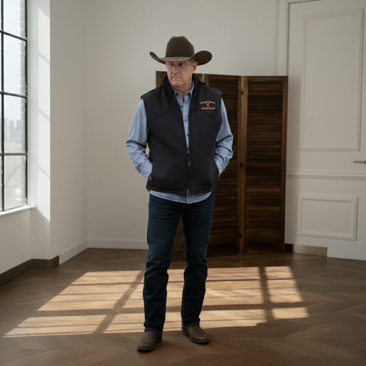 The model wears a black western vest with a denim shirt and cowboy hat in a warmly lit indoor scene.
