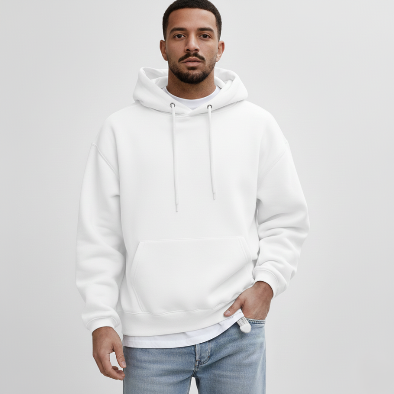Male model in a white pullover hoodie styled with jeans in bright studio lighting.