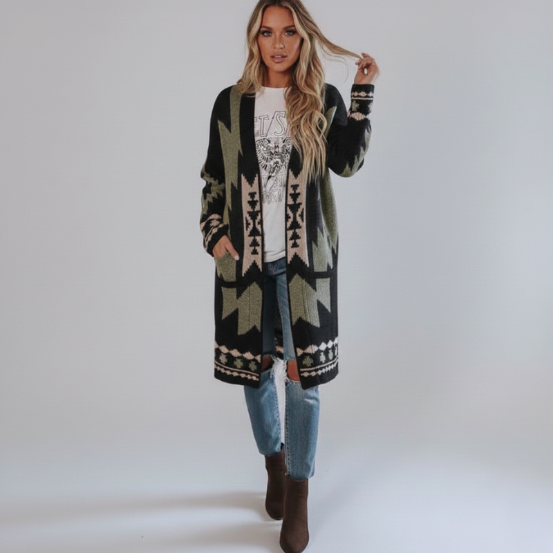 Woman wearing a long, patterned cardigan over a graphic t-shirt and jeans on a plain background