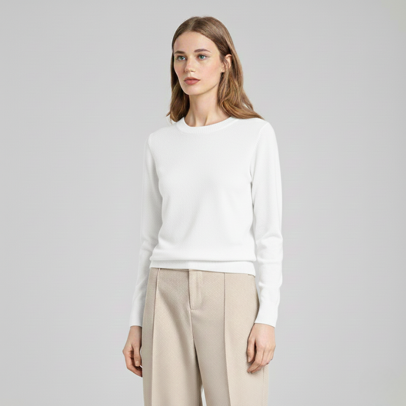 Female model in a white crewneck sweater standing against a plain background, highlighting a simple women’s knit top.